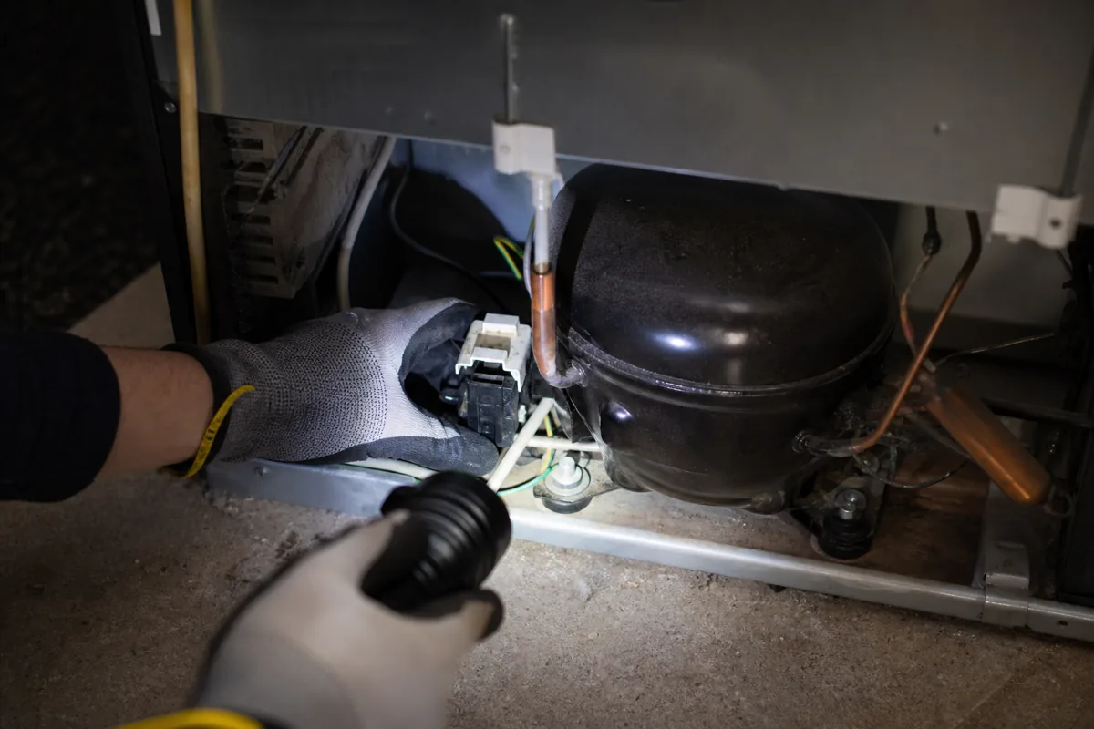 Checking a Whirlpool refrigerator's compressor area for a cooling problem.